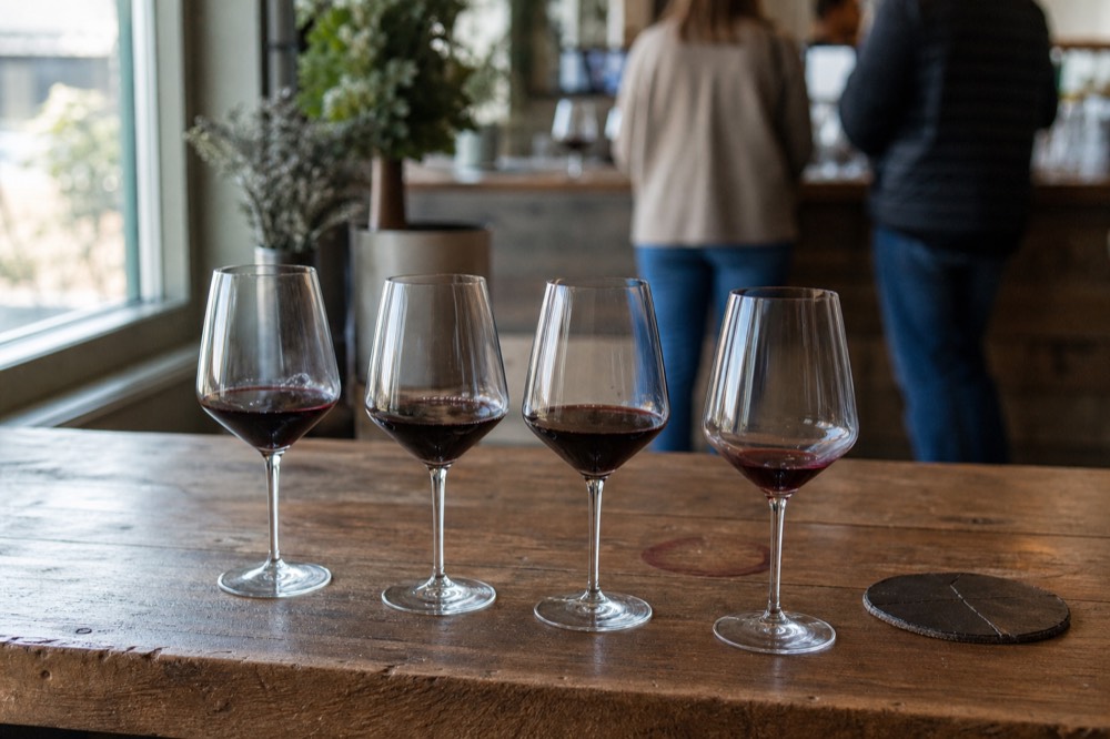 A tasting flight of red wines on a wooden tasting room counter