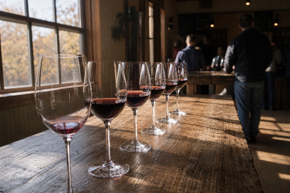 A tasting flight of red wine glasses lined up on a wooden tasting room bar