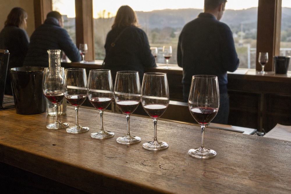 A tasting flight of red wines arranged on a wooden tasting room counter