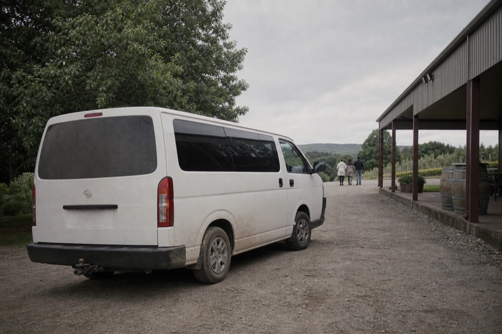 A passenger van parked on a gravel drive beside a winery building