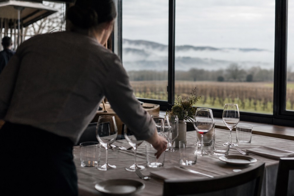 A Willamette Valley tasting room host setting glasses at a reservation table