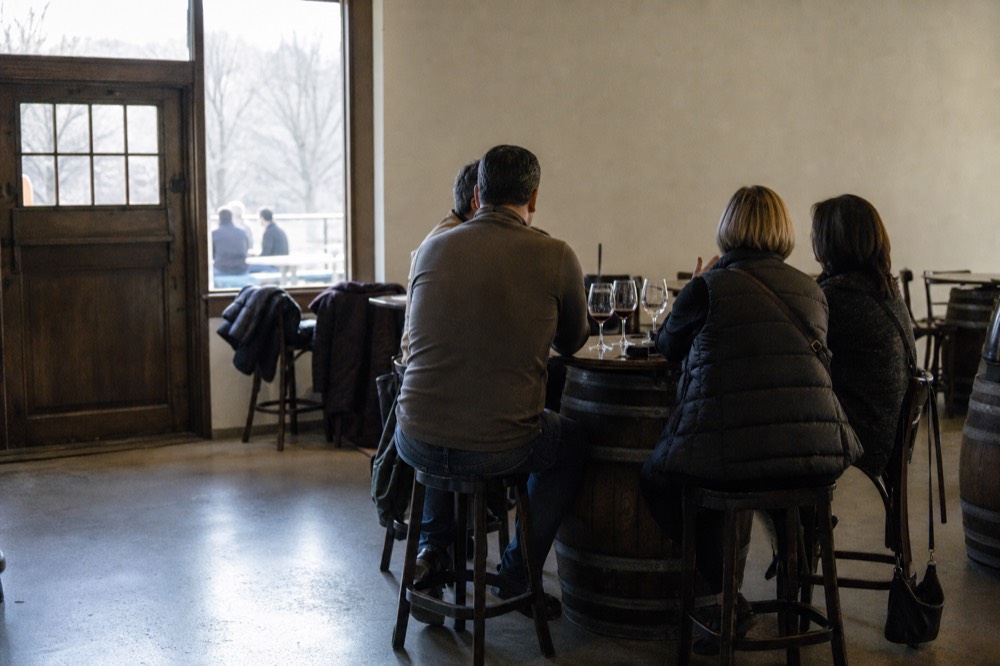 A quiet seated tasting room with a small group at a barrel table