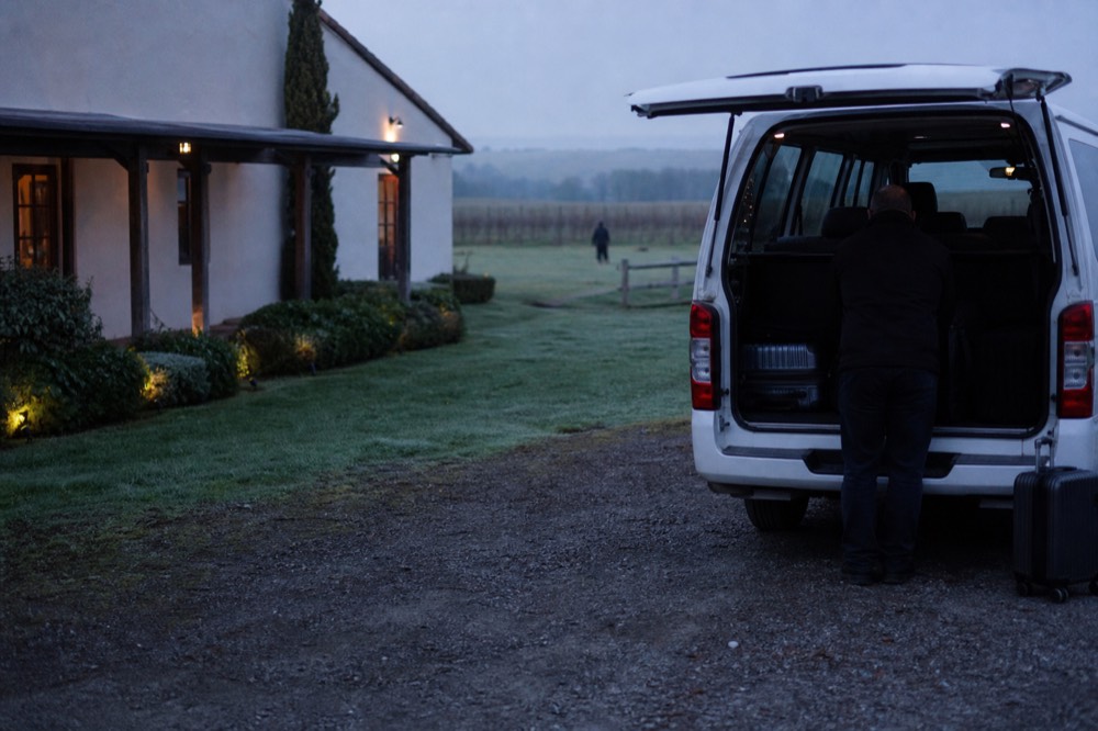 A driver loading luggage into a van outside a wine-country inn