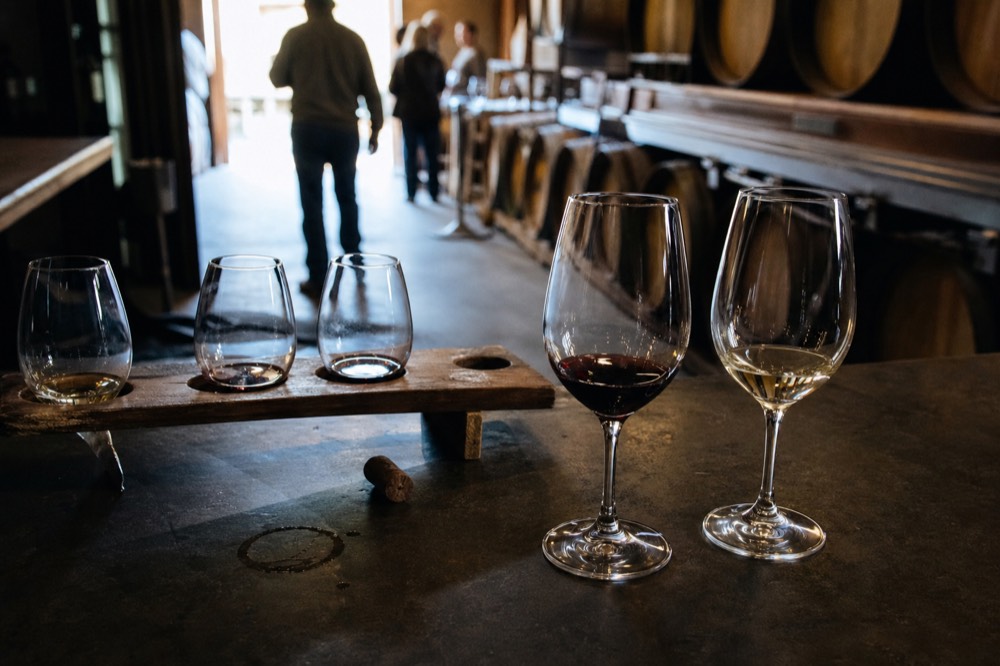 Two wine glasses beside a tasting flight on a winery barrel-room counter