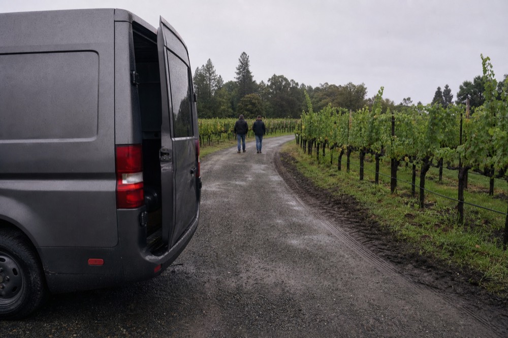 A passenger van parked at a winery entrance among vines